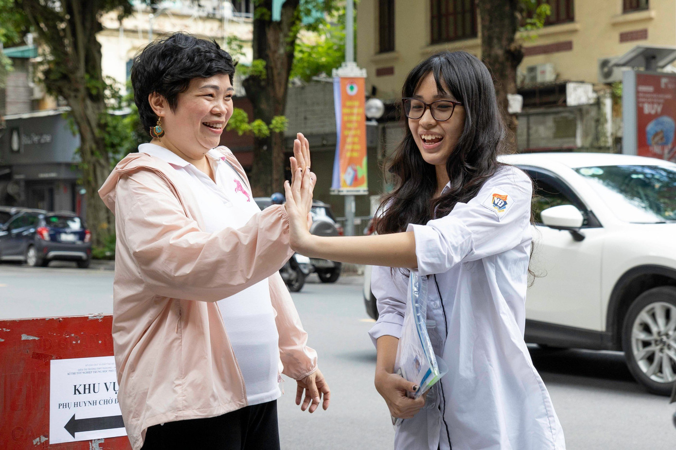 Cô Phan Hồng Giang đập tay chúc mừng con gái sau bài thi tổ hợp. Cô Giang chia sẻ: &quot;Thấy con và các bạn ra khỏi phòng thi đều rất là vui vẻ và tự tin, cô rất vui. Bạn nhà cô có mong muốn thi vào Trường Đại học Khoa học Xã hội &amp; Nhân văn, bạn ấy đã rất kiên trì, bền bỉ và nỗ lực trong quá trình học tập. Cô luôn đồng hành cùng bạn với vai trò là một người bạn, một người cố vấn để cho bạn có thể tìm hiểu về ngành nghề, môn học, nếu các bạn ý cần sự hỗ trợ nào thì mình có thể kết nối với các thầy cô để hỗ trợ và tư vấn.&quot; (Ghi nhận tại điểm thi Trường THPT Trần Phú - Hà Nội)