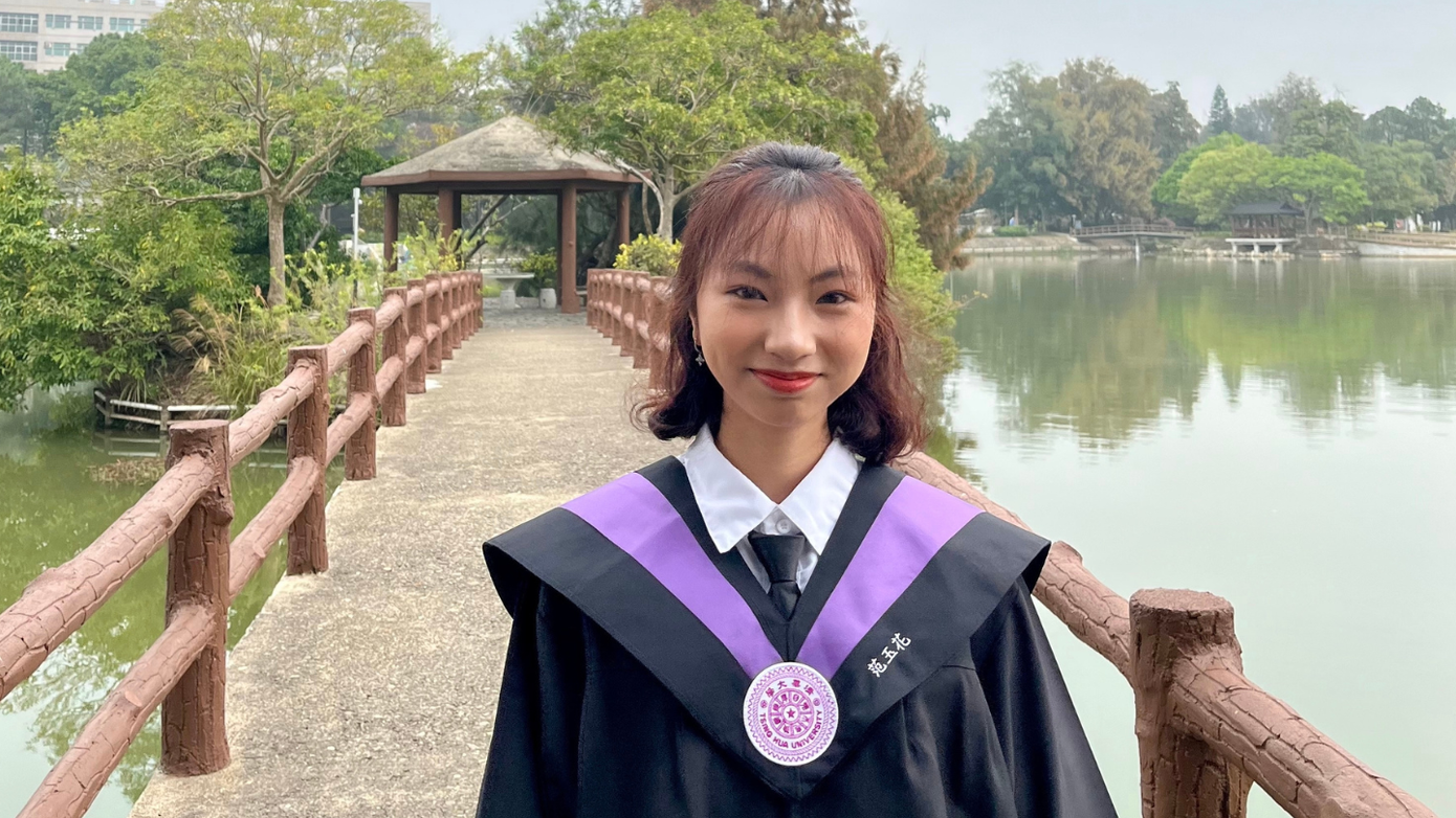 Ngọc Hoa diện lễ phục tốt nghiệp có thêu tên riêng bằng tiếng Trung ở cổ áo, chụp tại khuôn viên trường.