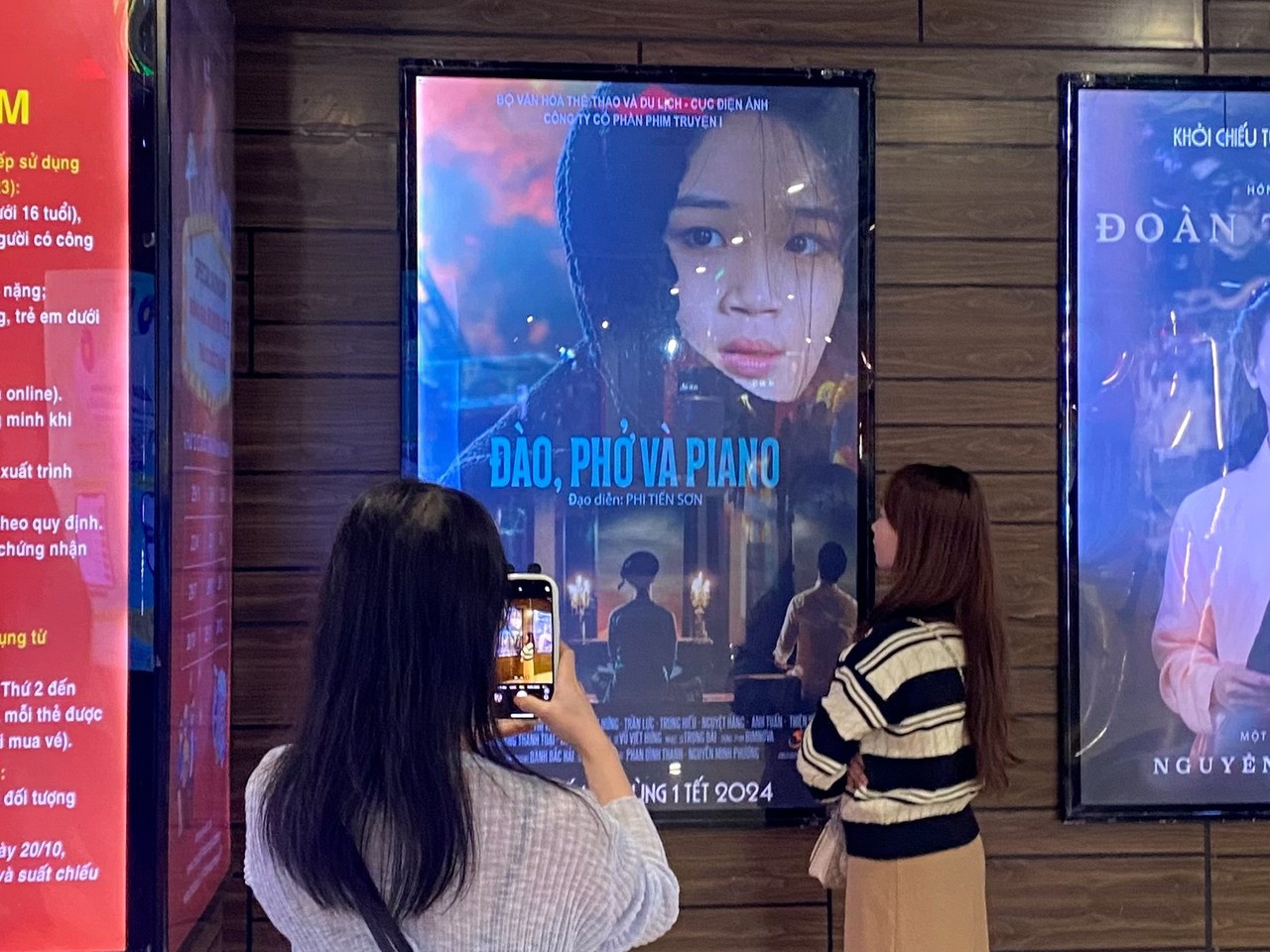 Khán giả trẻ chụp ảnh cùng poster phim Đào, phở và piano tại Trung tâm chiếu phim Quốc gia, tối ngày 22/2.