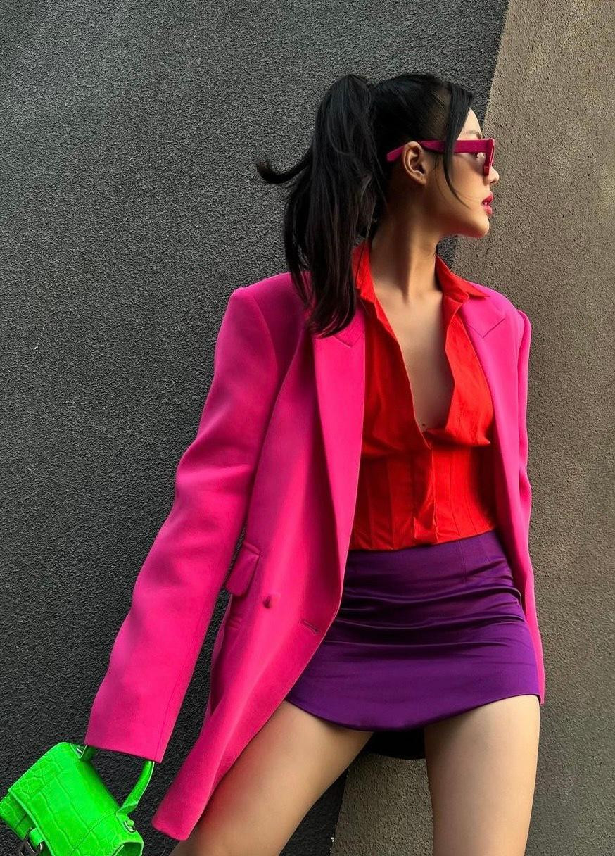 "Đồng chí" Khánh Linh "cháy phố" với sơ mi đỏ mặc trong phối cùng vest hồng và túi xách xanh neon rực rỡ.