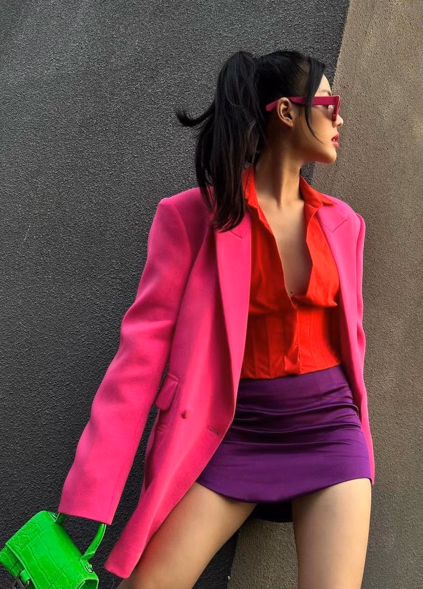 "Đồng chí" Khánh Linh "cháy phố" với sơ mi đỏ mặc trong phối cùng vest hồng và túi xách xanh neon rực rỡ.