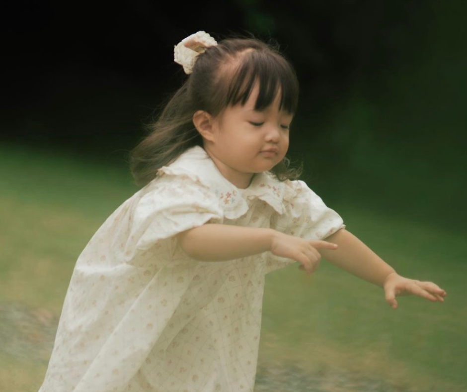 Nhóc tì diện đầm trắng, tóc cột nơ và tinh nghịch chơi đùa cùng bố mẹ.