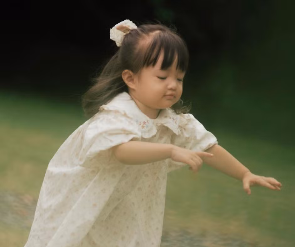 Nhóc tì diện đầm trắng, tóc cột nơ và tinh nghịch chơi đùa cùng bố mẹ.