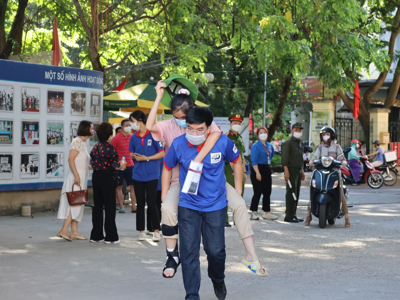 Em Hoàng Mai Linh, học sinh trường THCS Nguyễn Du (Nam Từ Liêm) bị bong gân bó chân 2 tháng nay, bố đưa đến trường, các tình nguyện viên cõng vào phòng thi số 02 trường THCS Việt Nam - Angieri