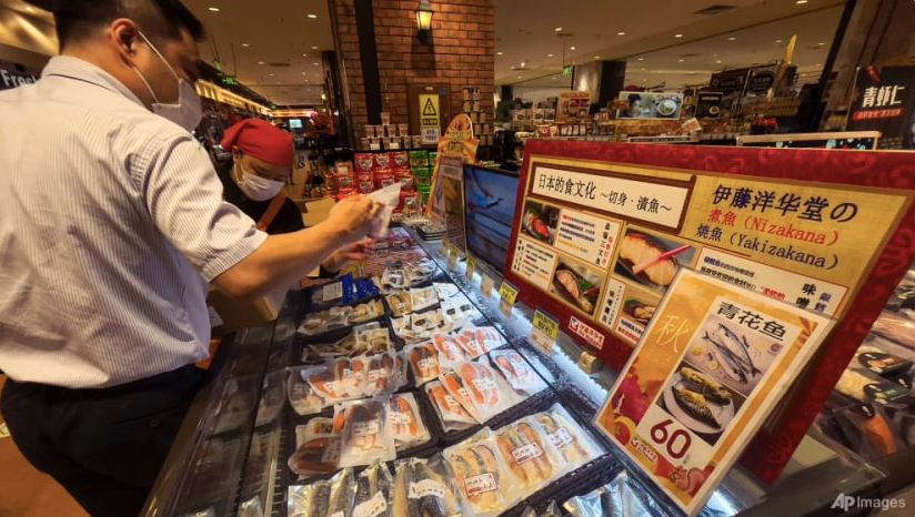 Công nhân xếp hải sản nhập khẩu từ Chile, Pháp và Canada gần tấm bảng và màn hình hướng dẫn cách nấu kiểu Nhật, tại một siêu thị Nhật Bản ở Bắc Kinh ngày 24/8. (Ảnh: AP)