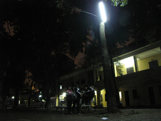 Một vài bạn học sinh ngồi nói chuyện dưới bóng đèn dưới sân trường. 