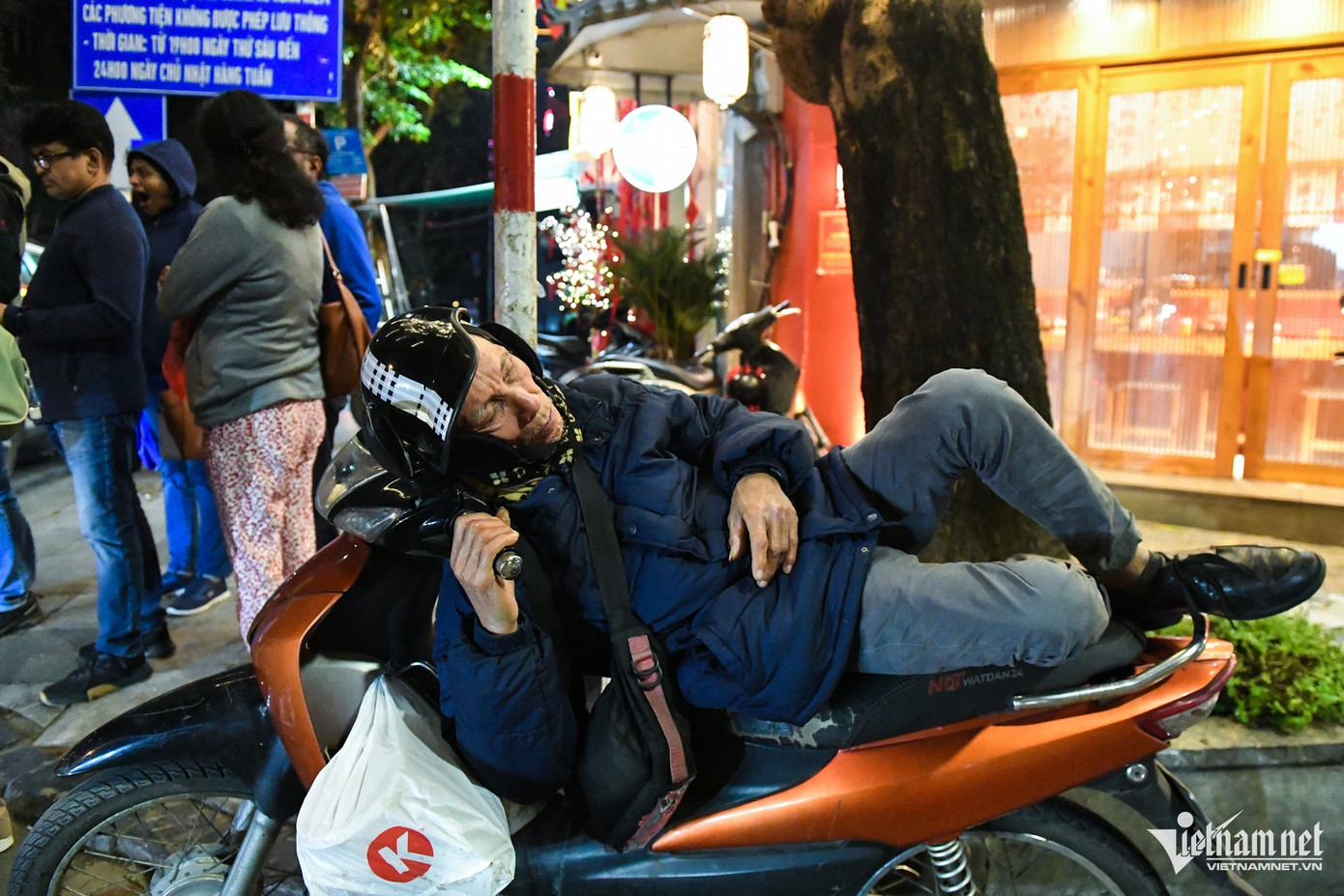 Đầu phố Lương Ngọc Quyến, một người lớn tuổi quàng khăn, đeo bịt tai, nằm lên yên xe máy trong bộ trang phục dày cộp. Đầu phố Lương Ngọc Quyến, một người lớn tuổi quàng khăn, đeo bịt tai, nằm lên yên xe máy trong bộ trang phục dày cộp.