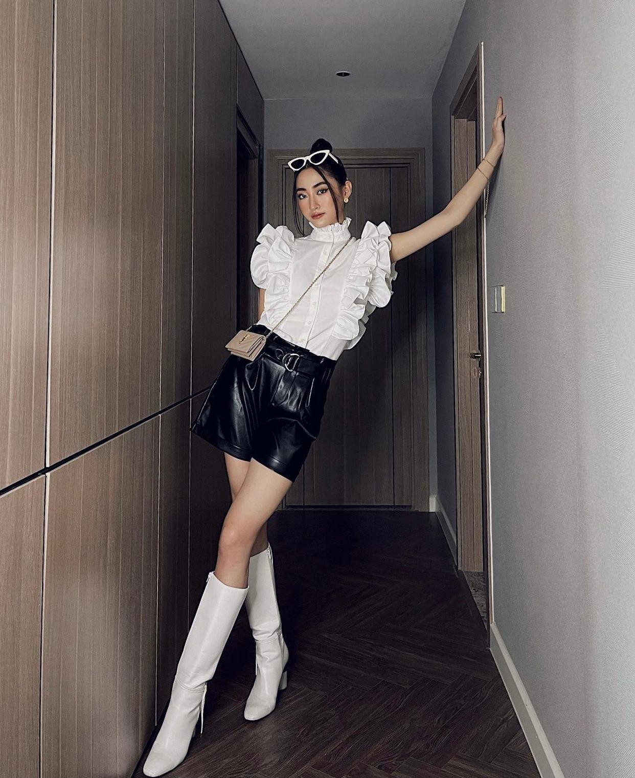 Người đẹp kết hợp áo bèo nhún điệu đà với chân váy da màu đen và đôi boot cao cổ màu trắng, khoe trọn đôi chân dài 1m22 trứ danh.