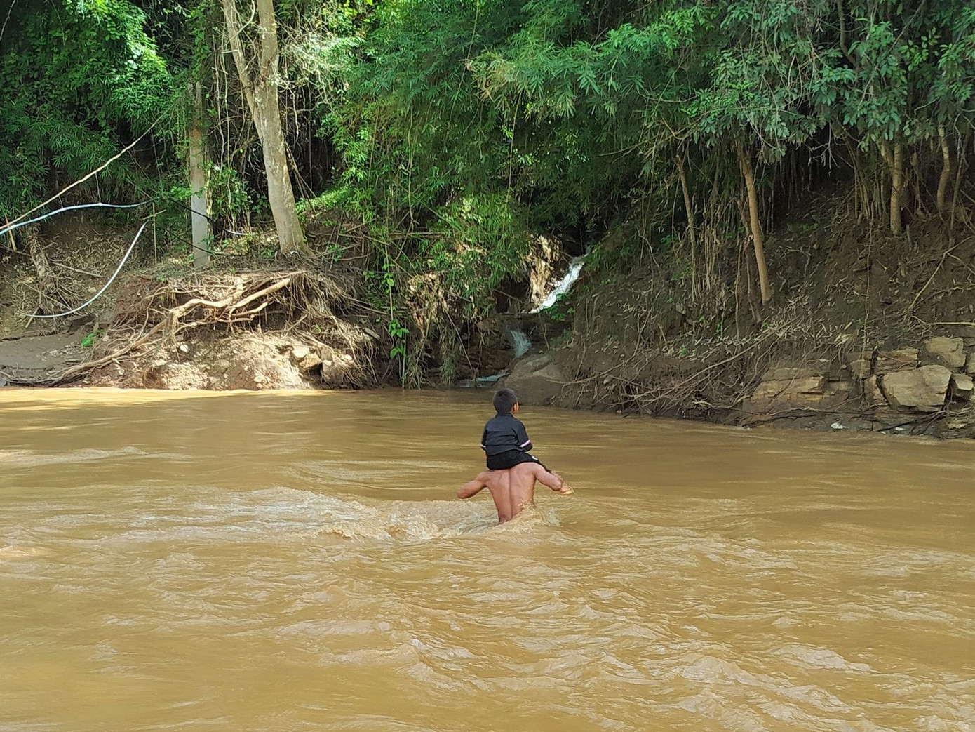 Người đàn ông đang cõng con trên vai, vượt qua dòng suối lớn.