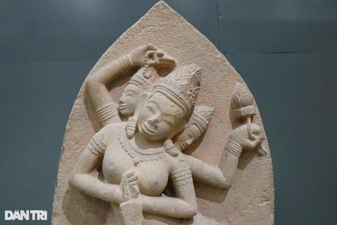 Phù điêu khắc nổi trang trí mặt chính diện; mặt sau lưng để trơn. Phù điêu được tạo dáng hình vòm cung nhọn, hình tượng thể hiện trong hình vòm cung là một vị nữ thần ngồi kiểu kiết già trên một tòa sen; thần có 3 đầu, mỗi đầu đều đội mũ chóp nhọn, trang trí 3 tầng hoa văn cánh sen; 4 cánh tay: cổ tay, bắp tay đều đeo những vòng trang sức…