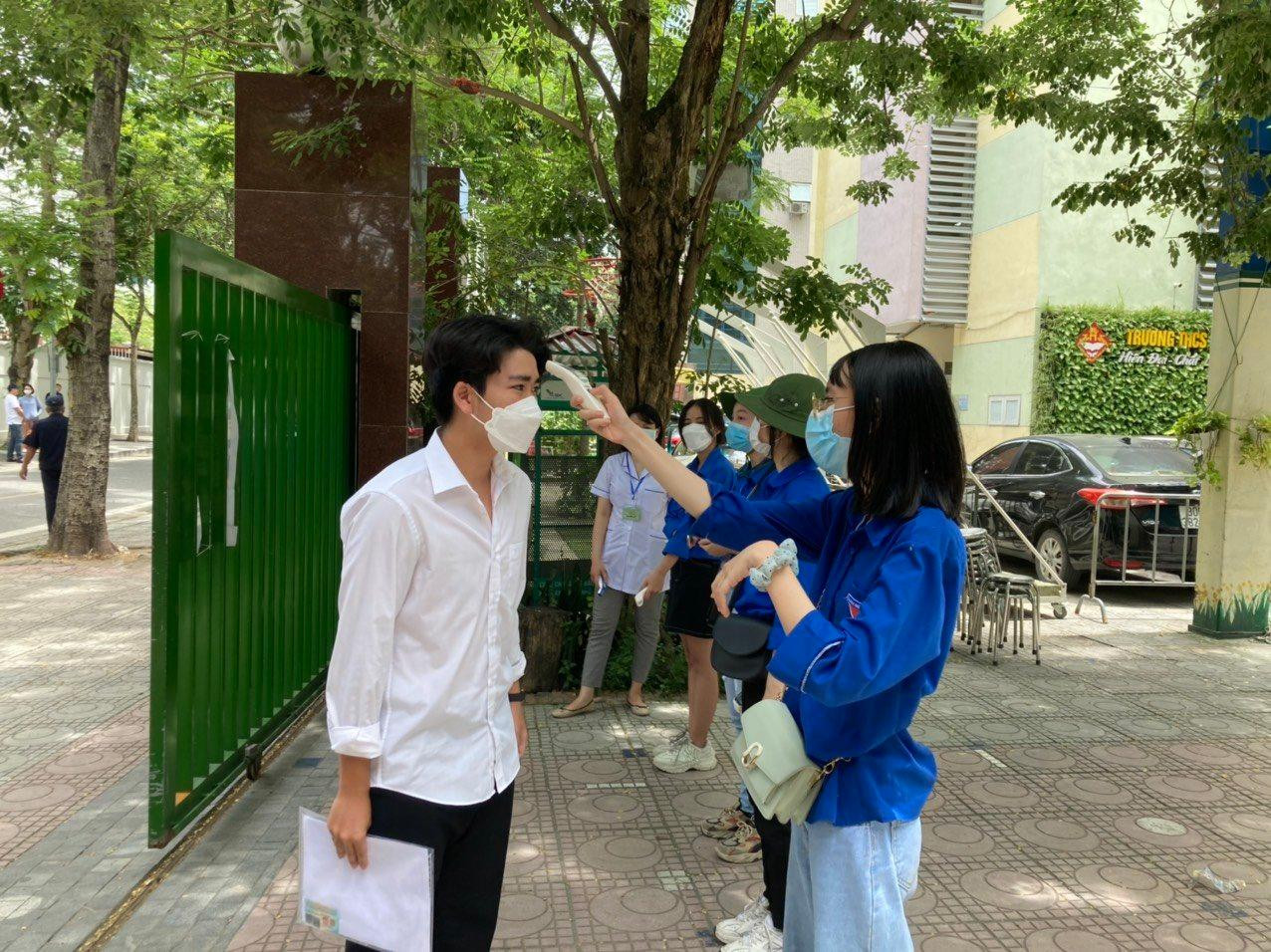 Thanh niên tình nguyện hỗ trợ đo nhiệt độ cho thí sinh tại điểm thi THCS Thăng Long, Ba Đình sáng ngày 19/6.