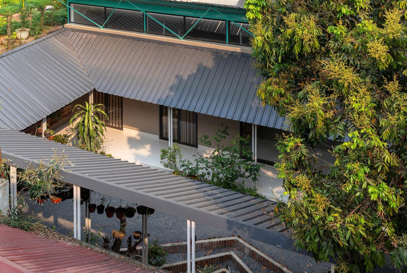 Một mái hiên bằng tôn được dựng lên xung quanh khoảng sân, kết nối với ngôi nhà, tạo ra vòng khép kín quanh sân để trồng hoa lan và cây cảnh.