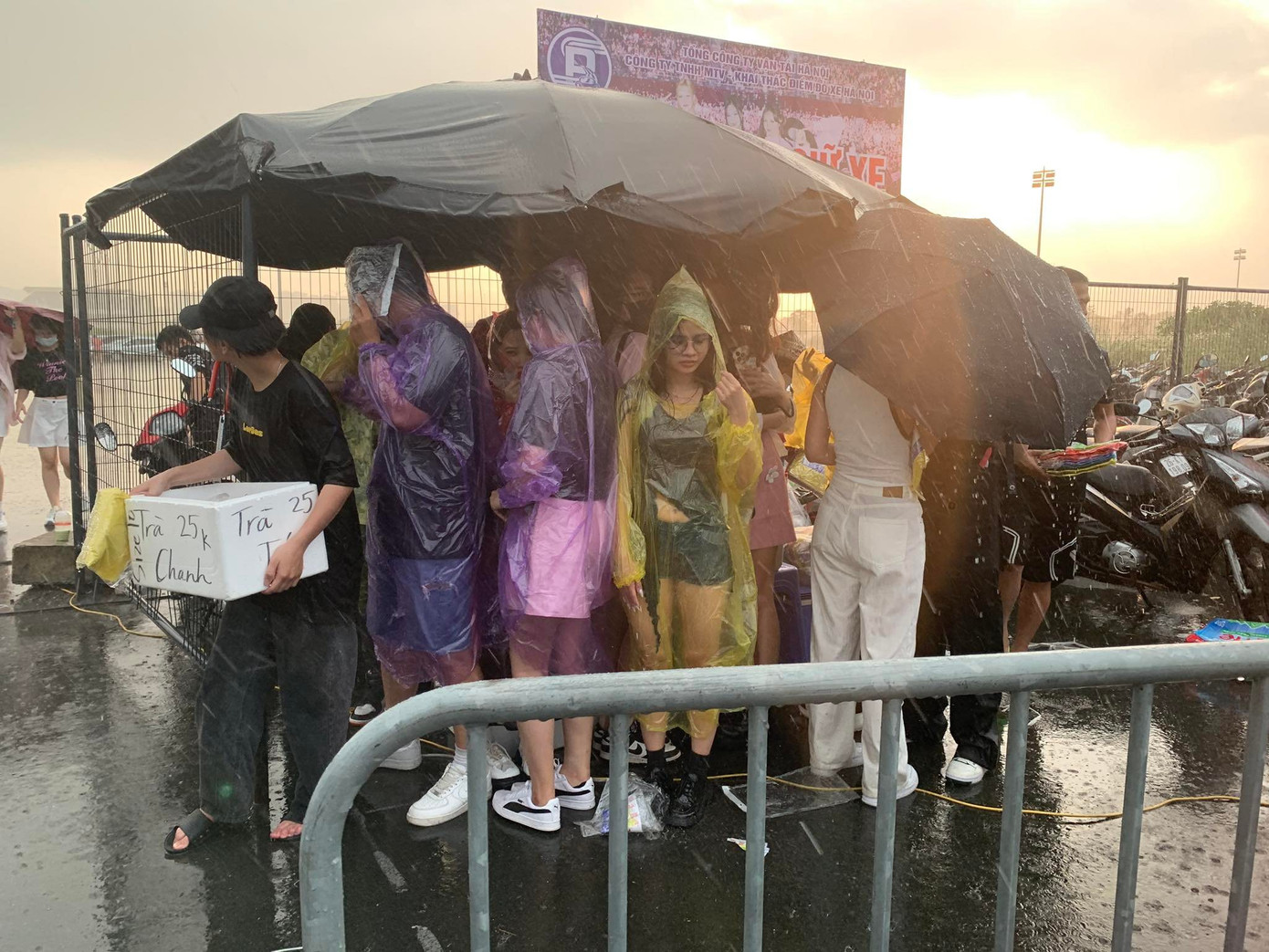 Mưa ngày càng nặng hạt, áo mưa tiện lợi dường như không đủ dày để che chắn cho người hâm mộ. Nhiều người tìm chỗ trú dưới tán ô dựng tạm.