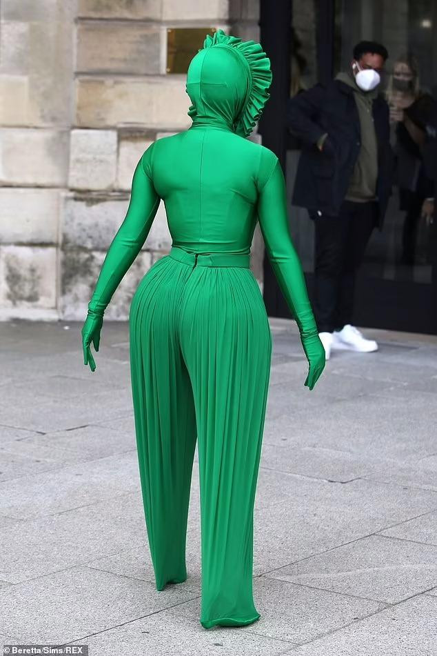 Thân trên là chiếc áo bó sát cơ thể với tay áo bao kín cả bàn tay và mũ trùm đầu. Người đẹp phối với quần xếp ly không một kẽ hở, trùm luôn cả giày cao gót. Cô còn đeo thêm kính râm có gọng xanh lá &quot;ton-sur-ton&quot; với trang phục.