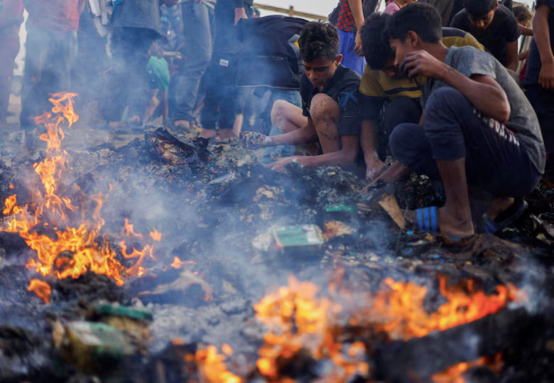Người Palestine tìm lại đồ ăn trong đám cháy sau cuộc không kích của Israel vào khu lều của người di tản. (Ảnh: Reuters) Người Palestine tìm lại đồ ăn trong đám cháy sau cuộc không kích của Israel vào khu lều của người di tản. (Ảnh: Reuters)