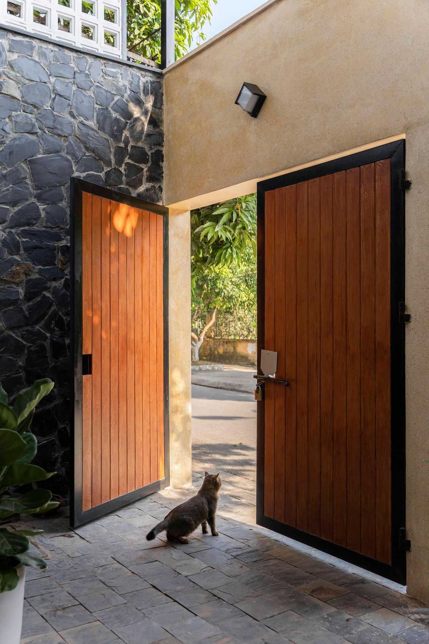 Sân trước nhà được ốp đá tự nhiên ở sàn và tường, tạo cảm giác gần gũi, thô mộc cho người sinh sống. Khu vực này vừa là khoảng đệm tránh khói bụi, vừa để gìn giữ cây xanh đã trồng từ hồi nhà cũ.