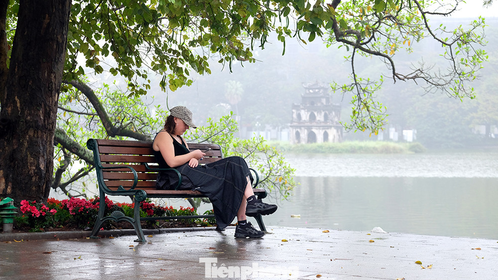 Du khách ngồi thư giãn bên Hồ Gươm buổi sáng sớm.