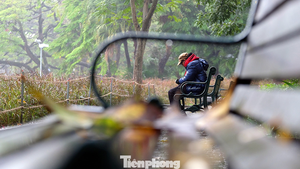 Một người đàn ông ngồi trên ghế đá nghe nhạc trong không gian mờ ảo bên Hồ Hoàn Kiếm.