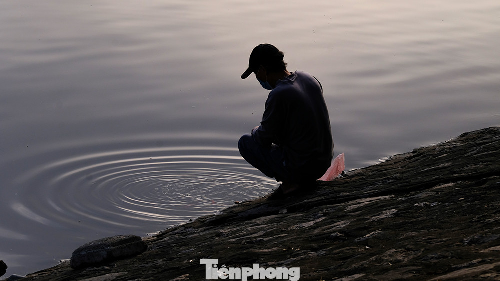 Người đàn ông ngồi nhìn đàn cá tung tăng bơi lội sau khi được ông thả xuống mặt hồ.