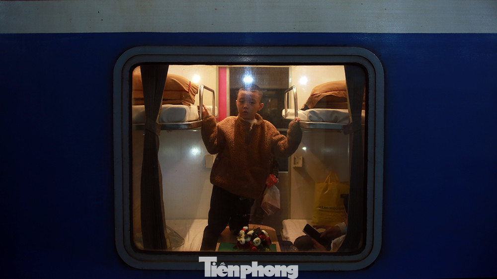 Một em bé đi cùng bố mẹ về quê ăn Tết nhìn qua khung cửa sổ trong khi đoàn tàu bắt đầu chầm chậm lăn bánh rời sân ga.