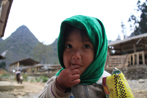 Một bé gái đang ăn bim bim gần chợ Sà Phìn. Tay em bé bầm tím đi vì lạnh. Ảnh: Trường Phong. 