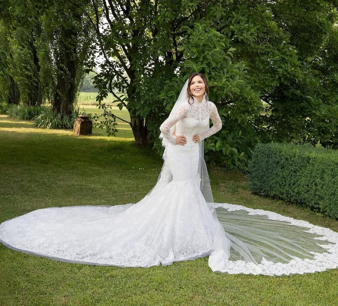 Bà Bezos bước vào lễ đường với váy cưới ren dài tay của Dolce & Gabbana. Chiếc váy có phần eo corset, cổ lọ và hàng nút từ cổ xuống sàn và kiểu dáng theo phong cách nàng tiên cá. Cô dâu đội thêm khăn voan viền ren dài. Theo Vogue, nữ MC đeo đôi hoa tai Dolce & Gabbana Alta Gioielleria Miracolo có bốn viên kim cương được cắt từ một viên đá duy nhất và khảm vàng trắng. Ảnh: Vogue. Bà Bezos bước vào lễ đường với váy cưới ren dài tay của Dolce & Gabbana. Chiếc váy có phần eo corset, cổ lọ và hàng nút từ cổ xuống sàn và kiểu dáng theo phong cách nàng tiên cá. Cô dâu đội thêm khăn voan viền ren dài. Theo Vogue, nữ MC đeo đôi hoa tai Dolce & Gabbana Alta Gioielleria Miracolo có bốn viên kim cương được cắt từ một viên đá duy nhất và khảm vàng trắng. Ảnh: Vogue.