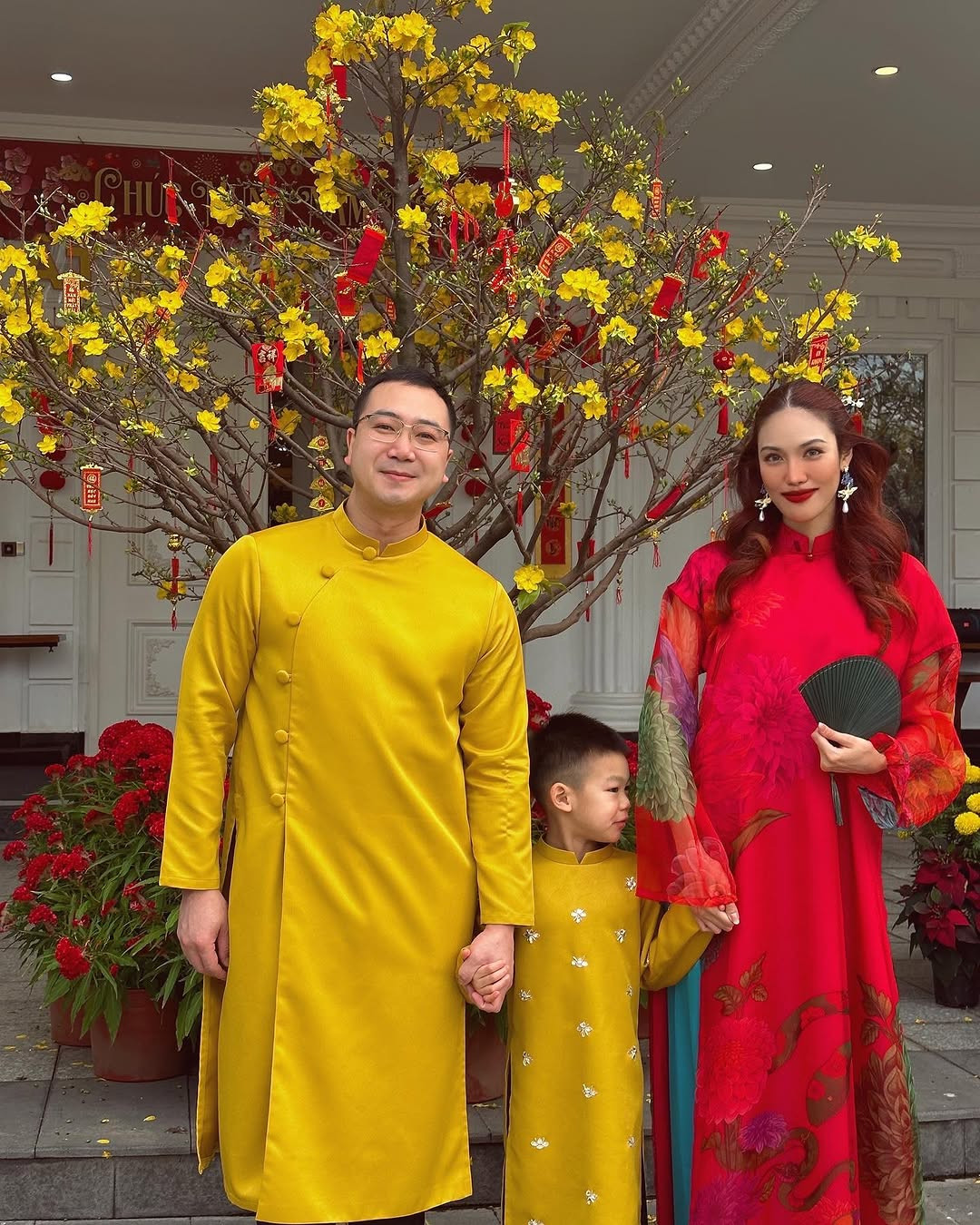 Lan Khuê cùng chồng và con trai chụp ảnh áo dài bên cây mai vàng nở rộ.