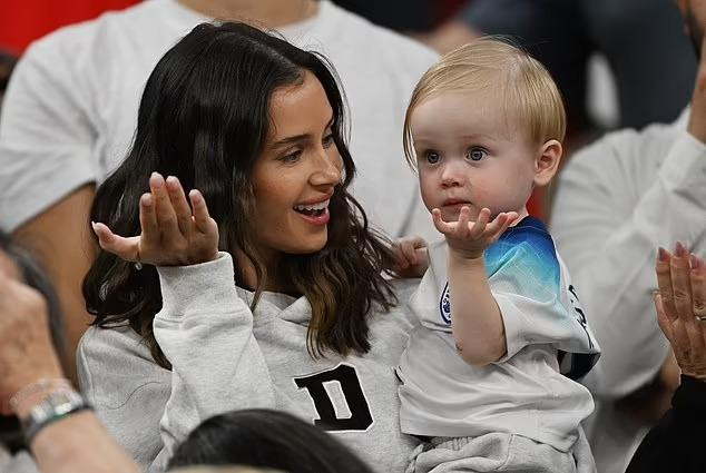 Bạn gái của tiền vệ James Maddison, Kennedy Alexa, hướng dẫn con trai cổ vũ cho đội nhà. Ảnh: Daily Mail.