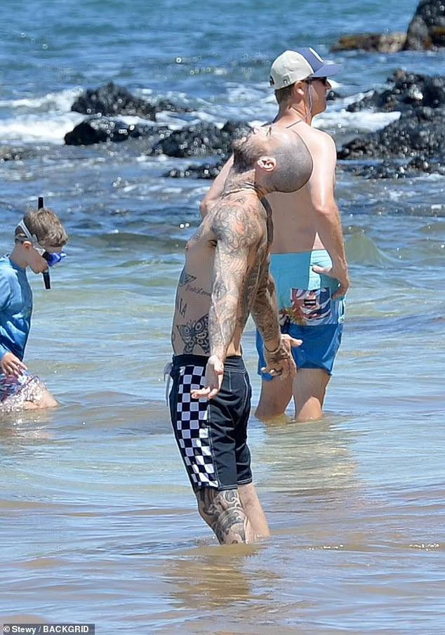 Adam nổi bật trên bãi biển với cơ thể phủ kín hình xăm. Ở tuổi U50, anh vẫn duy trì được thân hình rắn rỏi, cơ bắp.