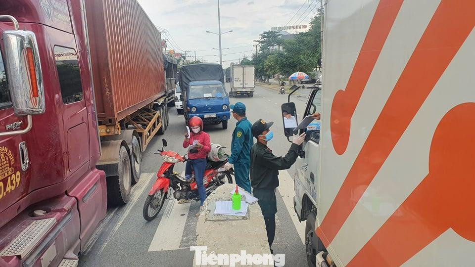 Tại chốt, nhiều xe chở hàng phải quay đầu do đi không đúng lộ trình hoặc vừa không có mã QR vừa không có giấy xét nghiệm còn hiệu lực đều quay đầu trở lại. Điều này dẫn đến xe cộ nối đuôi nhau, dồn ứ. Trong ảnh: Lực lượng chức năng quét mã và giấy thông hành của tài xế khi qua chốt