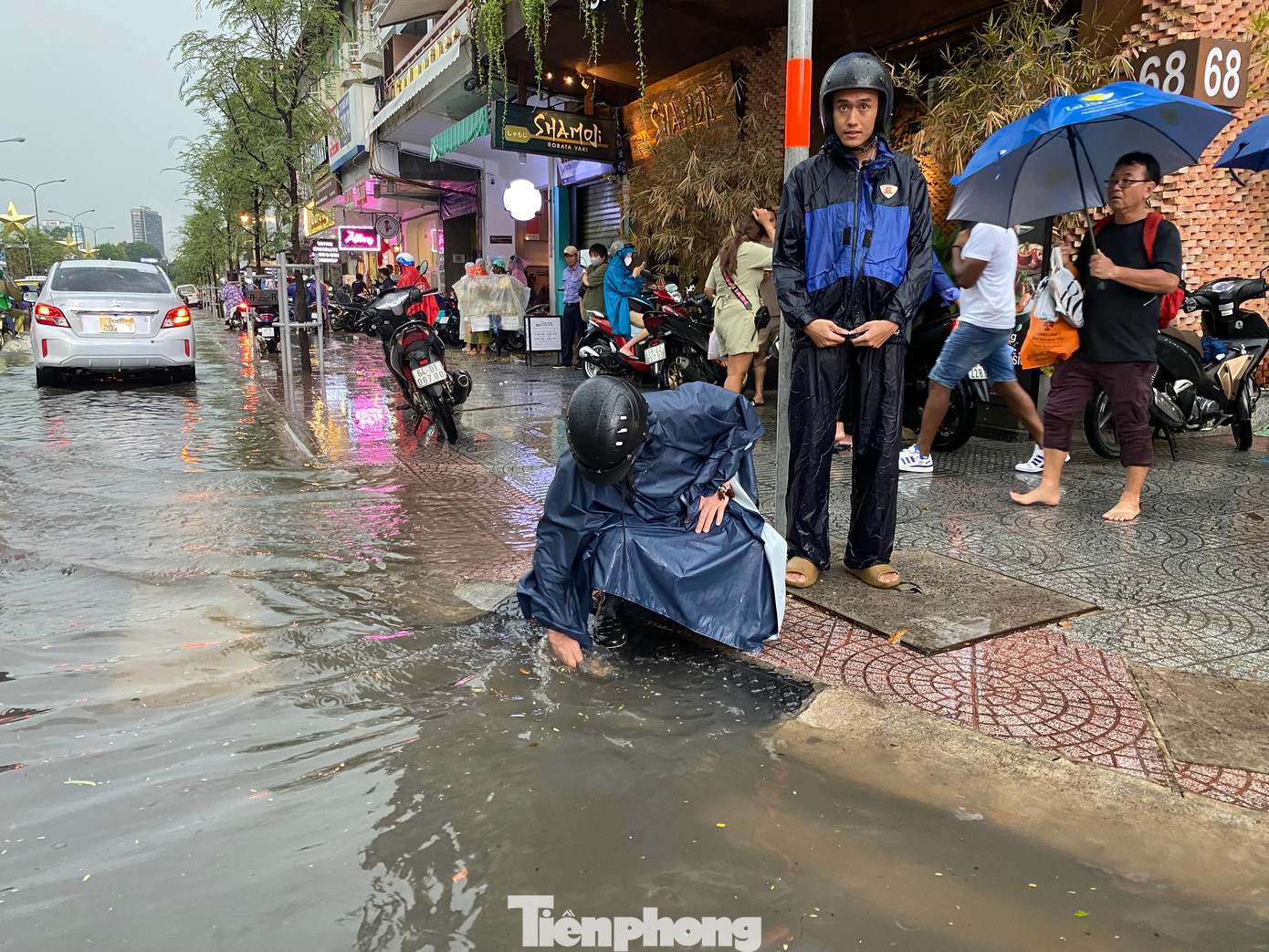 Người dân túc trực bên miệng cống trên đường Lê Lợi để vớt rác, khơi thông dòng chảy thoát nước.