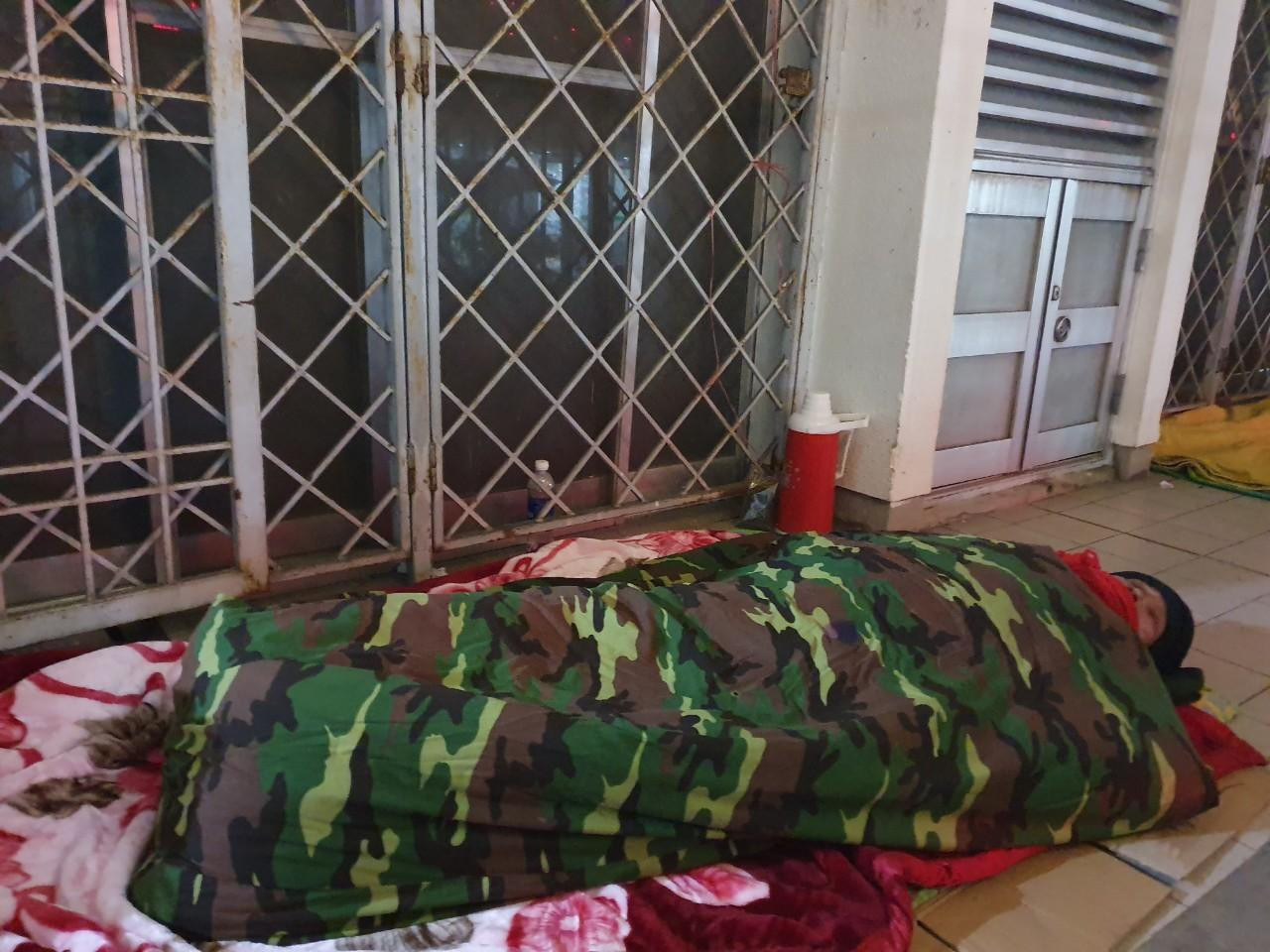 Gần đó, trên hành lang tòa nhà, anh Ly (quê ở Triệu Sơn, Thanh Hóa) cũng đã trải tấm bìa các tông và hai lớp chăn bông làm chỗ ngủ. Đêm qua, anh cùng người cháu đưa anh trai bị đột quỵ ra đây cấp cứu.