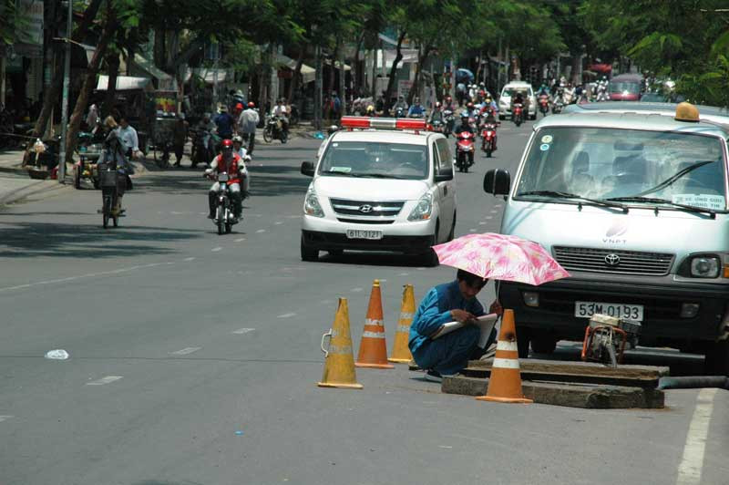 Người công nhân sửa cống phải mượn nhà dân gần đó một chiếc dù để tránh nóng trong khi làm việc