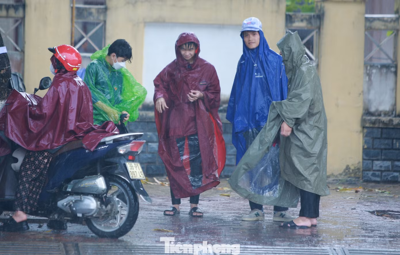 Nhiều phụ huynh đứng ngoài cổng trường chờ con em thi trong cơn mưa tầm tã.