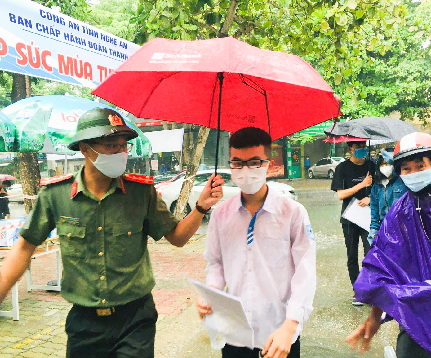 Đoàn viên, thanh niên tình nguyện nhường ô che mưa cho thí sinh.