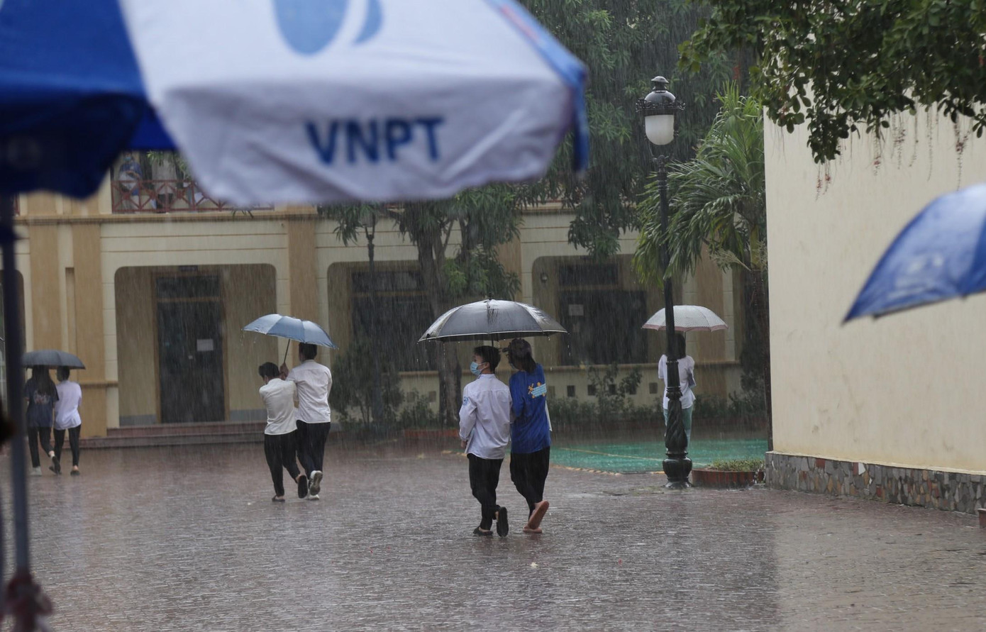 Từng nhóm thí sinh cùng che ô dù tránh mưa vào phòng thi.