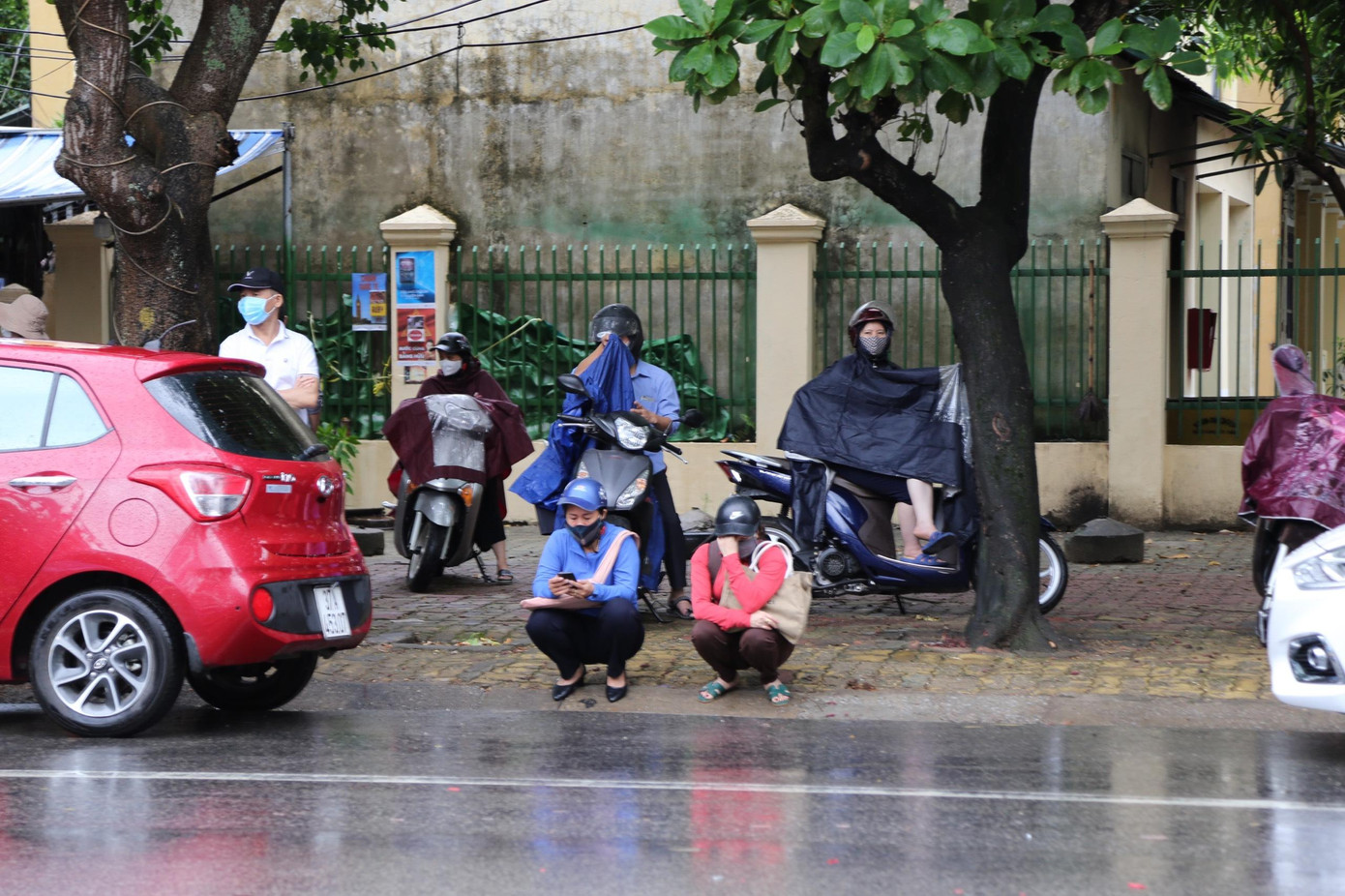 Phụ huynh &quot;đội mưa&quot; chờ đợi con thực hiện bài thi.