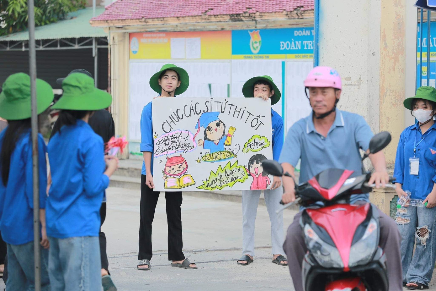 Đoàn viên trước điểm thi trường THPT Nguyễn Đức Mậu với bức tranh chúc các sĩ tử thi tốt mang lại niềm vui, động lực cho các thí sinh.