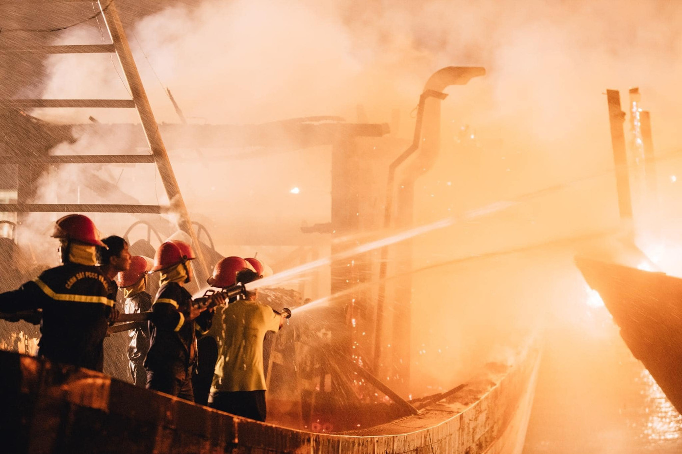 Lực lượng cảnh sát chữa cháy dùng vòi xịt chữa cháy tàu. Người dân xung quanh cũng vào hỗ trợ di dời tài sản và chữa cháy 5 tàu cá. Ảnh: Mạnh Tino.