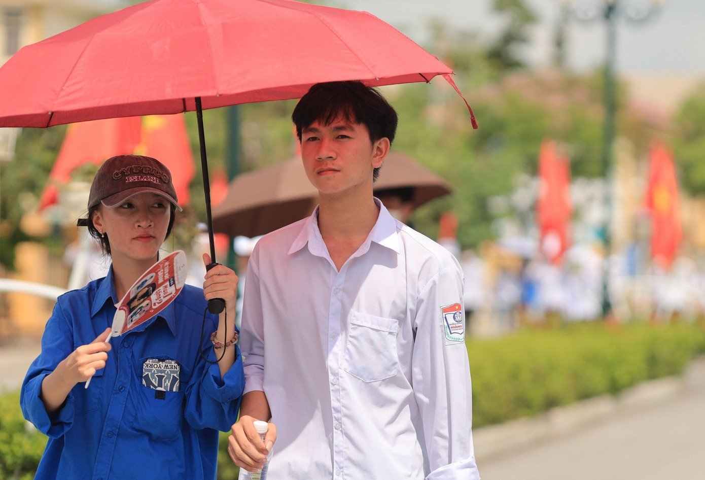 Trời nắng nóng, nữ tình nguyện viên mang theo ô che cho thí sinh khi bước vào điểm thi trường THPT Hoàng Mai. Ảnh: Trần Thanh.