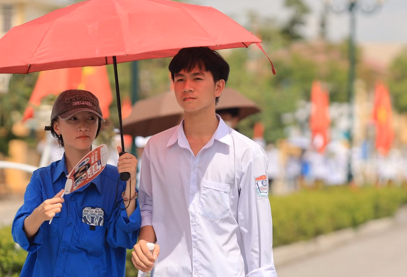 Trời nắng nóng, nữ tình nguyện viên mang theo ô che cho thí sinh khi bước vào điểm thi trường THPT Hoàng Mai. Ảnh: Trần Thanh.