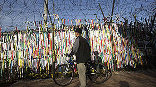 Một người đàn ông Hàn Quốc đang xem những mảnh giấy đề nguyện ước tái thống nhất đất nước ghim trên hàng rào dây thép gai ngăn biên giới hai miền ở Paju. Ảnh: AP