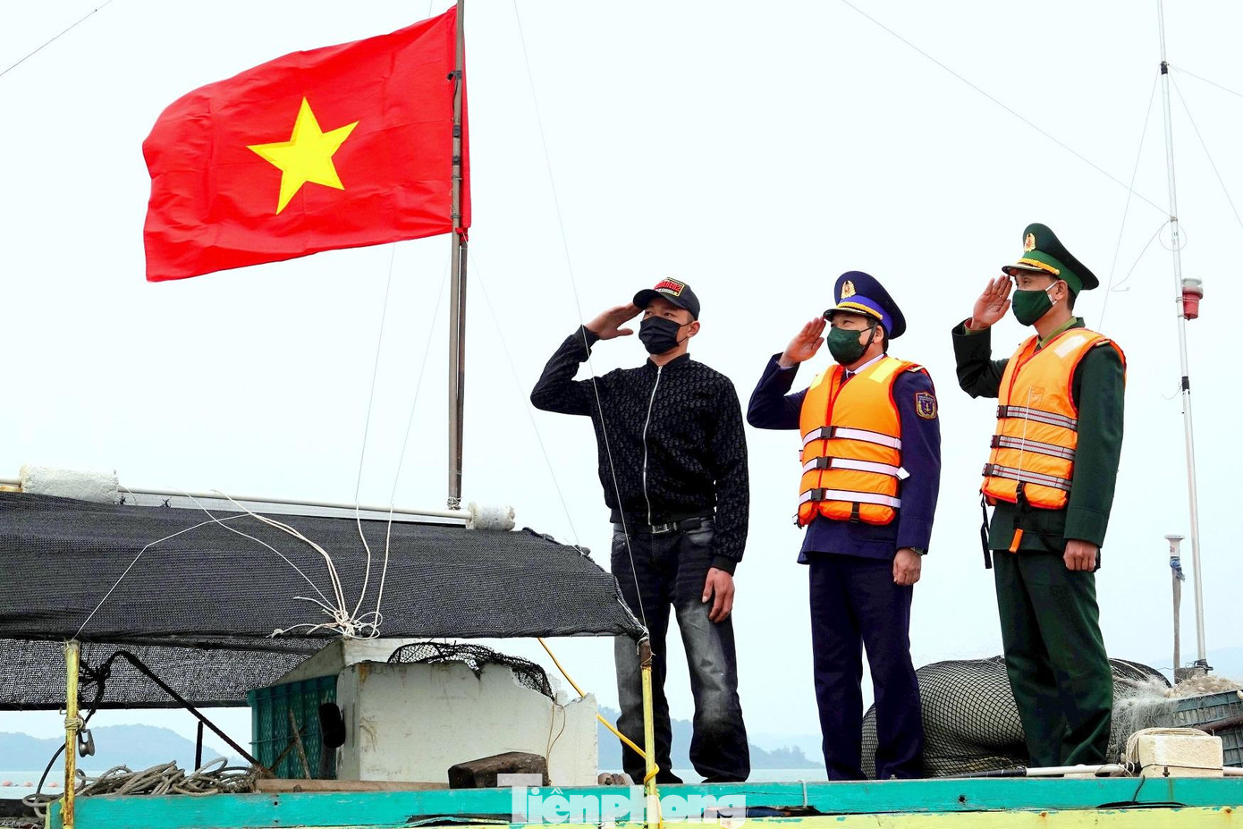 Chiến sĩ Vùng Cảnh sát biển 1 và Đồn Biên phòng Quan Lạn cùng ngư dân chào lá cờ Tổ quốc mới do Ban tổ chức chương trình và báo Người lao động trao tặng