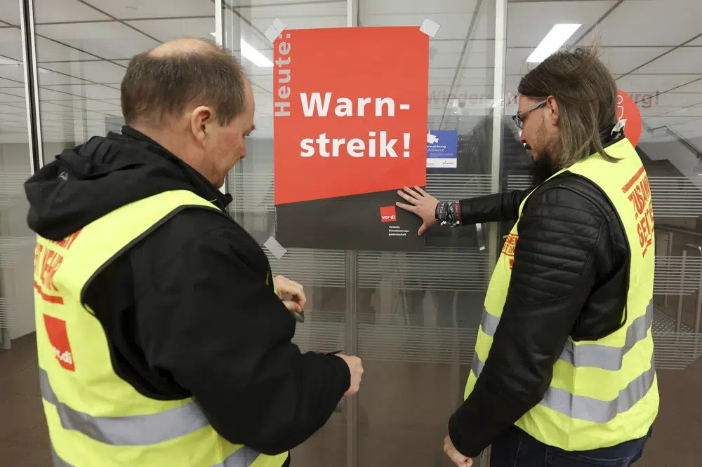 Các đại diện của công đoàn người lao động dán một tấm áp phích có nội dung "Cảnh báo đình công!" trên cửa kính ở sân bay Hamburg. Ảnh: AP