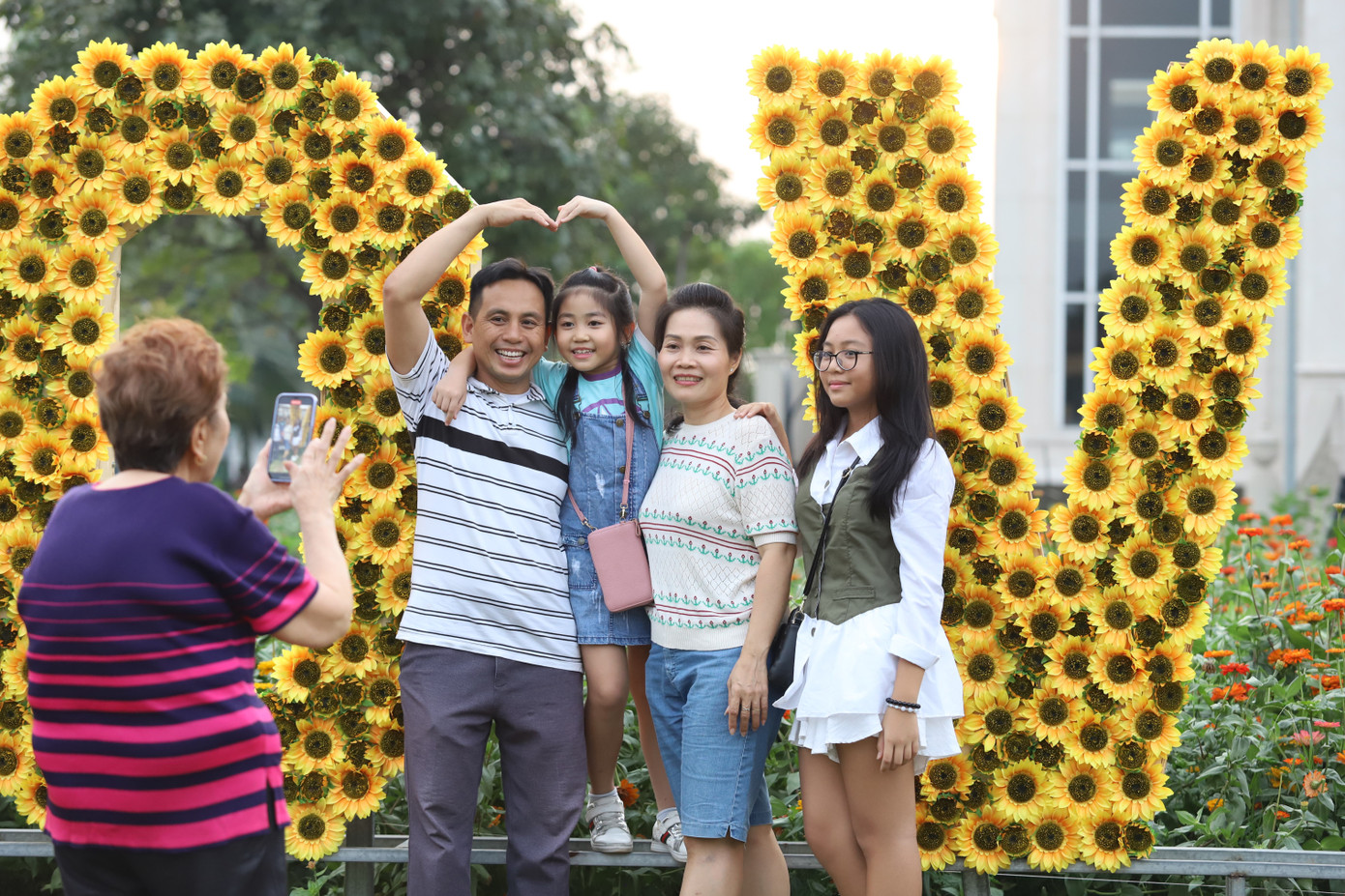 Một gia đình nhiều thế hệ chụp ảnh vui vẻ tại một tiểu cảnh hoa hướng dương.