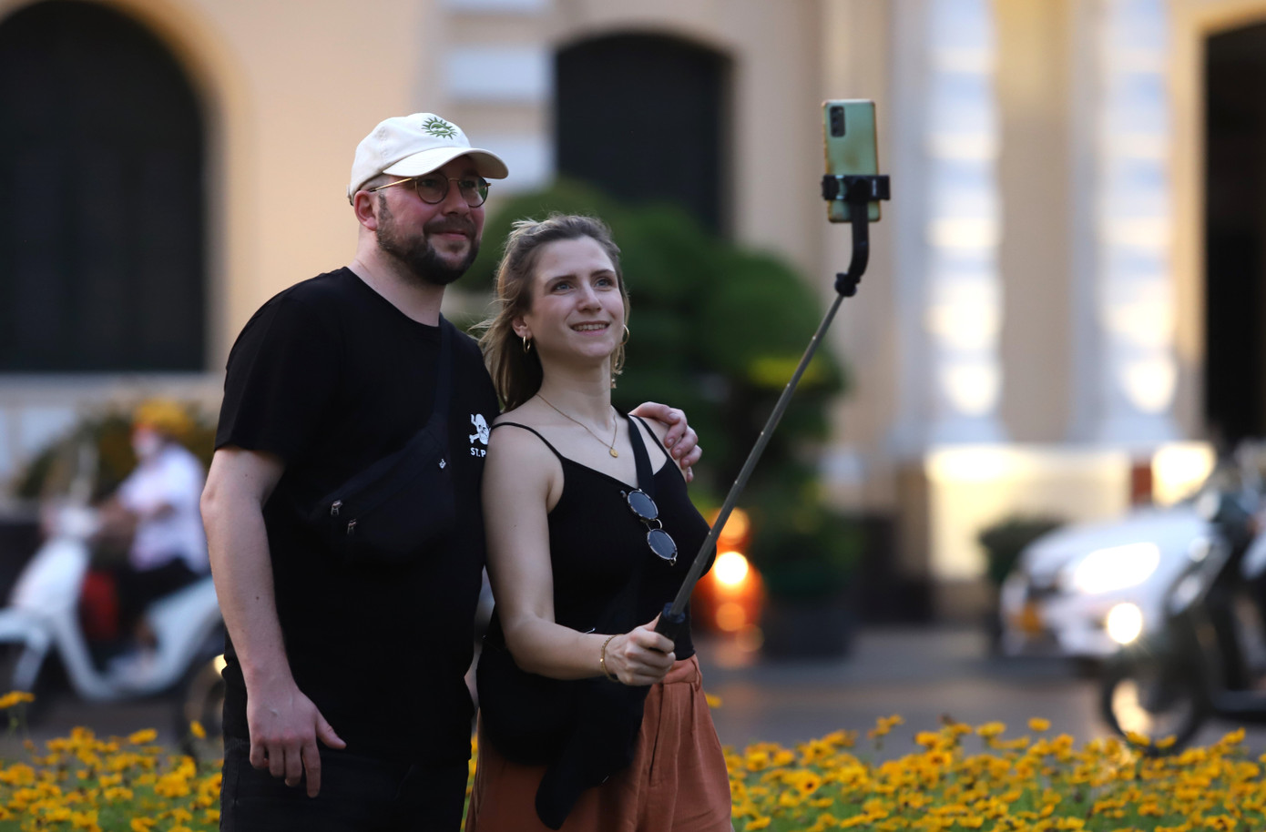 Hai vị khách nước ngoài chụp ảnh với bối cảnh tòa nhà UBND TPHCM phía sau lưng.