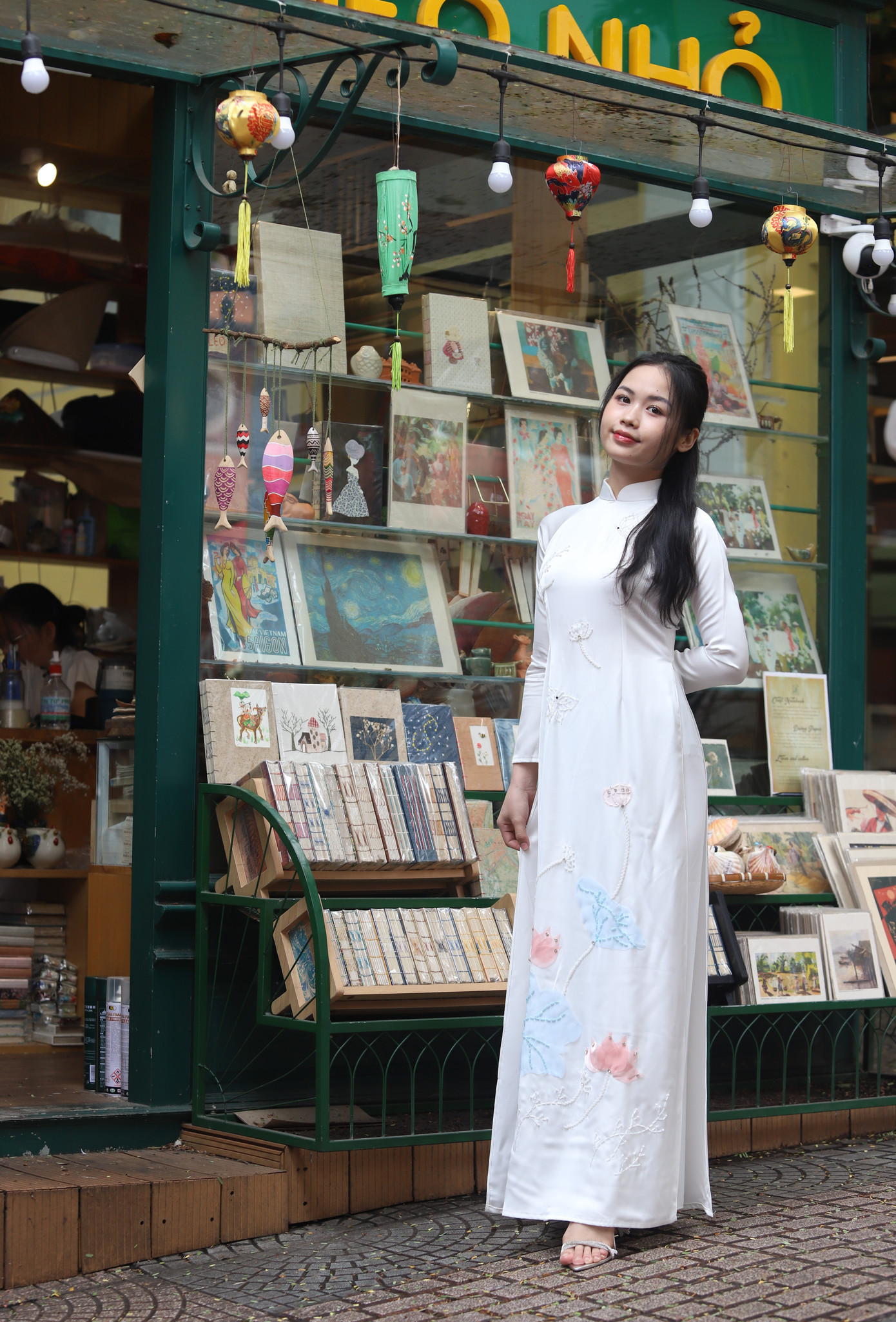 Thiếu nữ duyên dáng chụp ảnh bên một quày văn phòng phẩm tại đường sách. Thiếu nữ duyên dáng chụp ảnh bên một quày văn phòng phẩm tại đường sách.