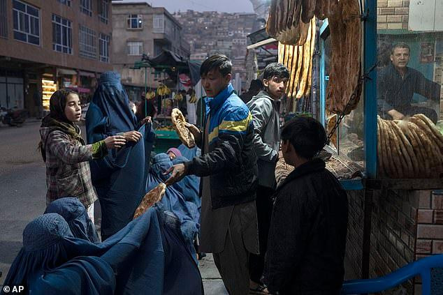 Một nam thanh niên chia bánh mì cho phụ nữ và trẻ em ở thủ đô Kabul (Afghanistan). Chi phí sinh hoạt ở Afghanistan đã gia tăng nhanh chóng sau khi Taliban lên nắm quyền vào ngày 15/8. Ảnh: AP