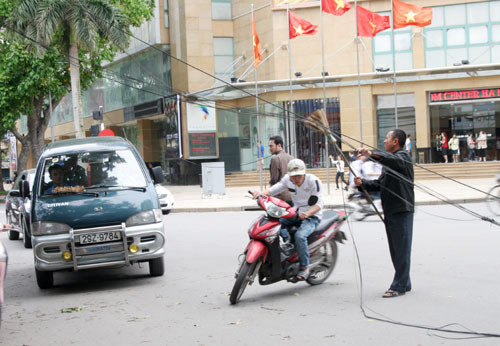 Một người dân tìm cách thu gọn các sợi dây điện và nâng dây điện lên để tạo lối đi