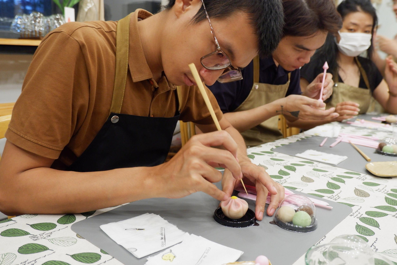 Khải đang hướng dẫn các bạn trẻ trong một workshop làm bánh. Khải đang hướng dẫn các bạn trẻ trong một workshop làm bánh.